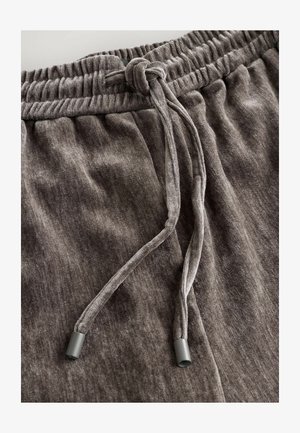 Grijze sweatpants van zacht materiaal met een elastische tailleband en een trekkoord, met een geknoopt strikje en subtiele textuur.
