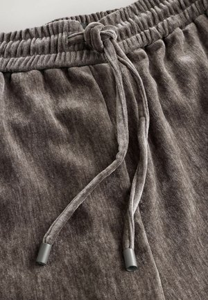 Pantaloni de trening gri dintr-un material moale, cu talie elastică și șnur, având un nod legat și o textură subtilă.