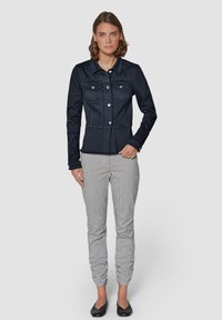 Donkerblauwe denimjas met twee borstzakken, vijf zilveren knopen en een getailleerde pasvorm. Gecombineerd met zwart-wit geblokte broek.