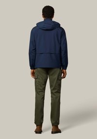 Tmavomodrá nepremokavá bunda s kapucňou, mäkká tkanina, elastické manžety a cargo nohavice v olivovo zelenej farbe. Hnedé semišové topánky dopĺňajú outfit.