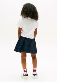 T-shirt bianco, gonna a pieghe blu navy con orlo testurizzato, calze a righe rosse e blu, e sneakers bianche con accenti blu navy.