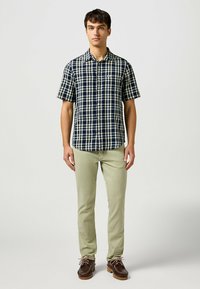 Camisa a cuadros de manga corta en azul marino y crema, con un collar abotonado. Combinada con pantalones verde claro y zapatos marrón con cordones.