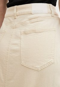 Helle beige Jeansrock mit glatter Textur, ausgestattet mit einer Gesäßtasche, sichtbaren Nähten und einem Markenlabel am Bund.