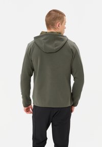 Dunkelolivgrüne Kapuzenjacke aus weichem, strukturiertem Stoff, mit Kapuze und schmaler Passform, kombiniert mit schwarzen Hosen. Sauberes, schlichtes Design.