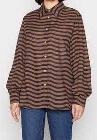 Camicia a righe marrone e blu con chiusura a bottoni, colletto classico e maniche a sbuffo. Realizzata in tessuto liscio, con polsini arrotondati.