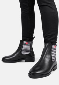 Czarne skórzane botki za kostkę z elastycznymi panelami w wzór houndstooth i małym akcentem w postaci czerwonego serca. Wytrzymała podeszwa i smukły fason.