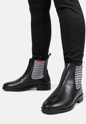 Czarne skórzane botki za kostkę z elastycznymi panelami w wzór houndstooth i małym akcentem w postaci czerwonego serca. Wytrzymała podeszwa i smukły fason.