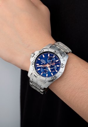 Montre en acier inoxydable argenté avec un cadran bleu, des accents en or rose, trois sous-cadrans et un bracelet à maillons. Présente de grands index horaires.