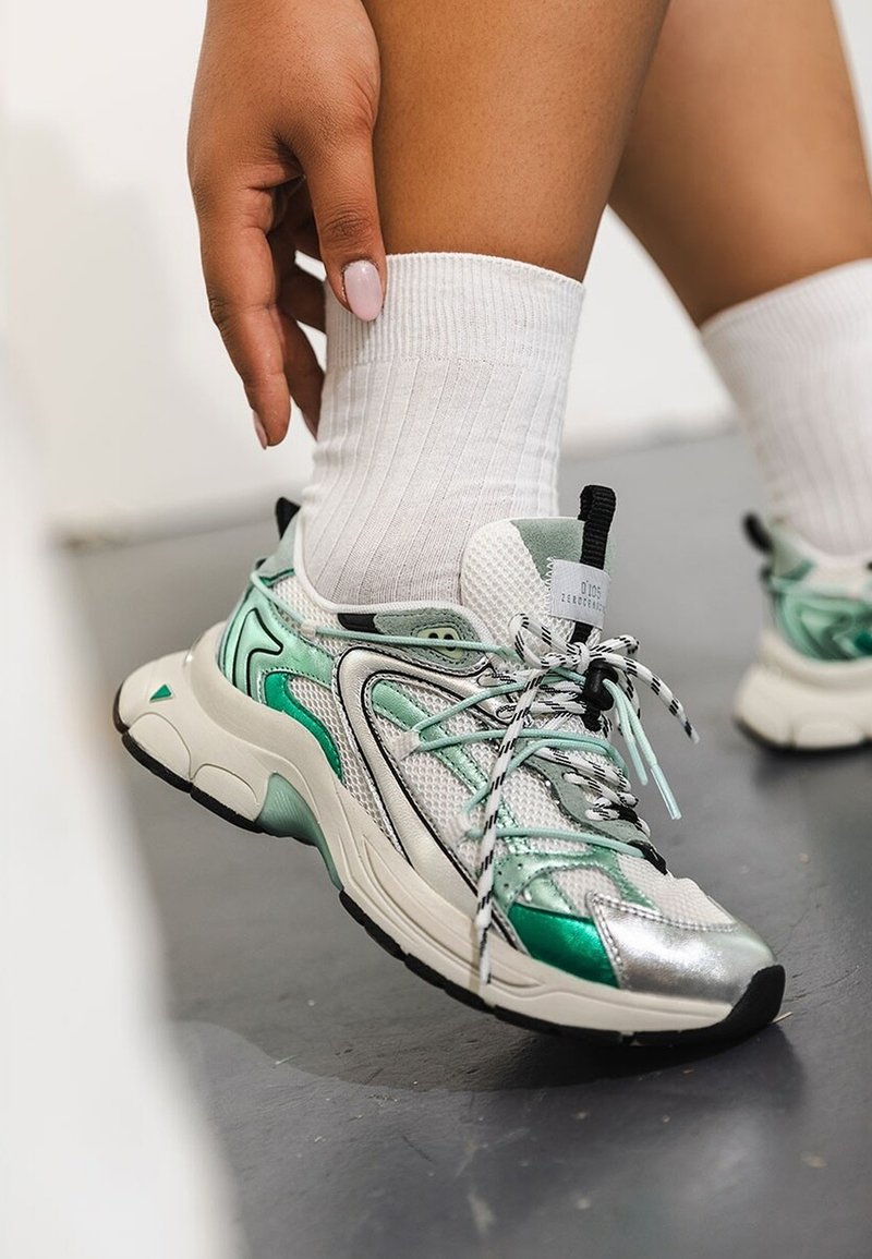 Scarpe sportive con una combinazione di materiali argento, bianco e verde menta. Parte superiore in mesh testurizzato, punta arrotondata e lacci a righe. Calze bianche a coste.