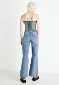 Denim corset top with vertical seams, blue wide-leg jeans, and platform shoes with a leopard print. Back view with visible tattoos.