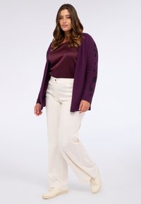 Lila kofta med blommönster broderat på ärmarna, bärs över en vinröd topp, matchas med vita vida byxor och krämfärgade sneakers.