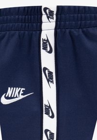 Τα σκούρα μπλε τζόγκερς από απαλό ύφασμα διαθέτουν λευκή ελαστική μέση και πλαϊνή ρίγα με επαναλαμβανόμενα μαύρα λογότυπα Nike, ενισχύοντας τη σύγχρονη αθλητική εμφάνιση.