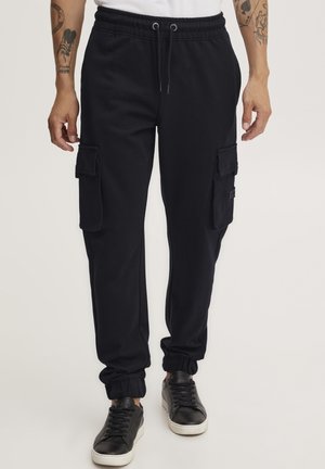Black cotton cargo joggers with elastic cuffs, drawstring waist, side pockets, and stitched detailing. Worn with black sneakers.