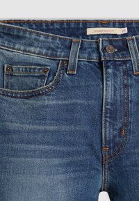 Jeans in denim blu con design a gamba bootcut, caratterizzati da una finitura sbiadita, cuciture arancioni e una tasca frontale con dettagli metallici.