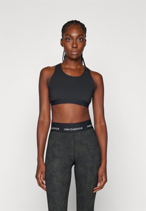 Svart sports-bh med brede stropper og glatt tekstur, kombinert med mørke leggings med mønster som har en svart livlinje med "new balance"-logo.