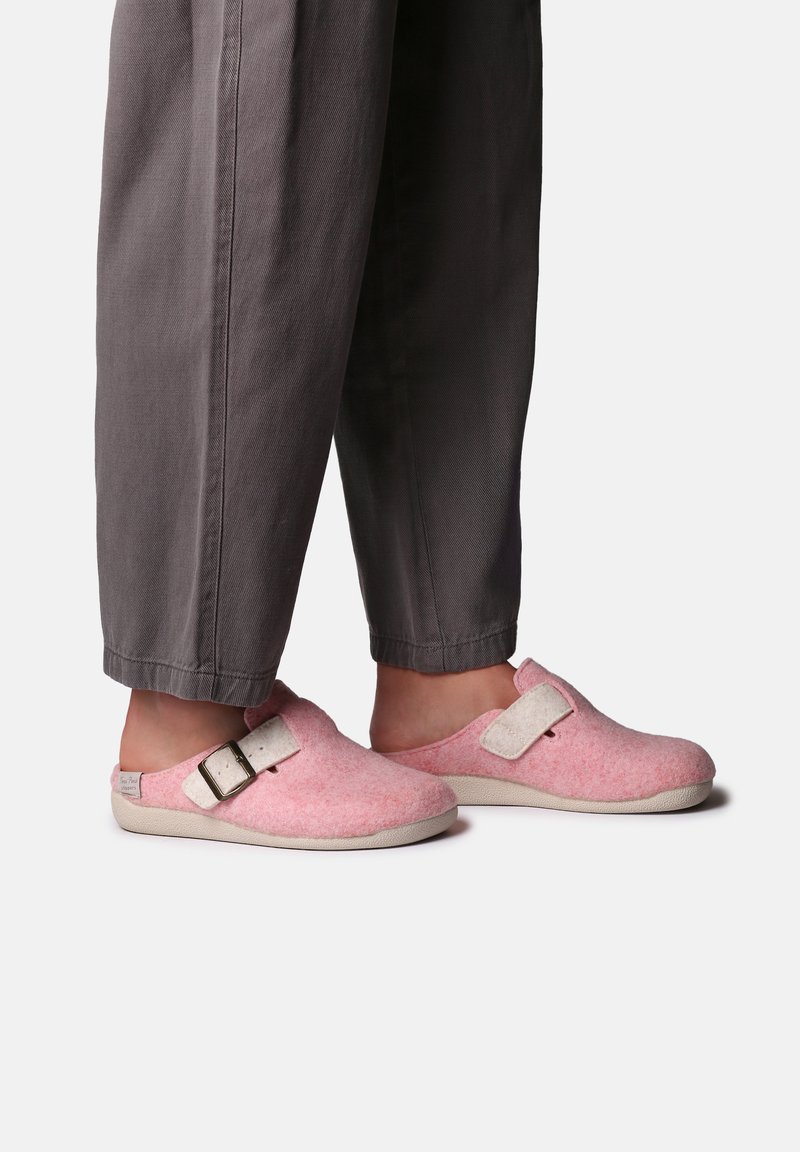 Pink felt clogs with a white strap and buckle detail, featuring a round toe design and textured surface, paired with gray trousers.