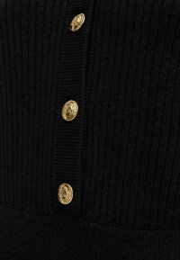 Μαύρο ριμπ ύφασμα με τρία κάθετα διακοσμητικά χρυσά κουμπιά, που φέρουν λεπτομερή ανάγλυφα σχέδια.