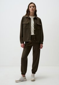 Olijfgroene gecoördineerde outfit met een knoopjasje met twee voorzakken en bijpassende joggingbroek met elastische boorden.