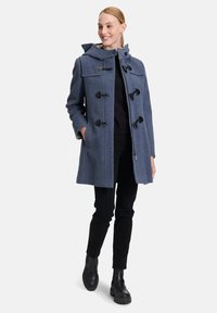 Kék gyapjú keverék kabát kapucnival, pöcök zárakkal és oldalsó zsebekkel. Slim fekete nadrággal és masszív fekete csizmával párosítva.