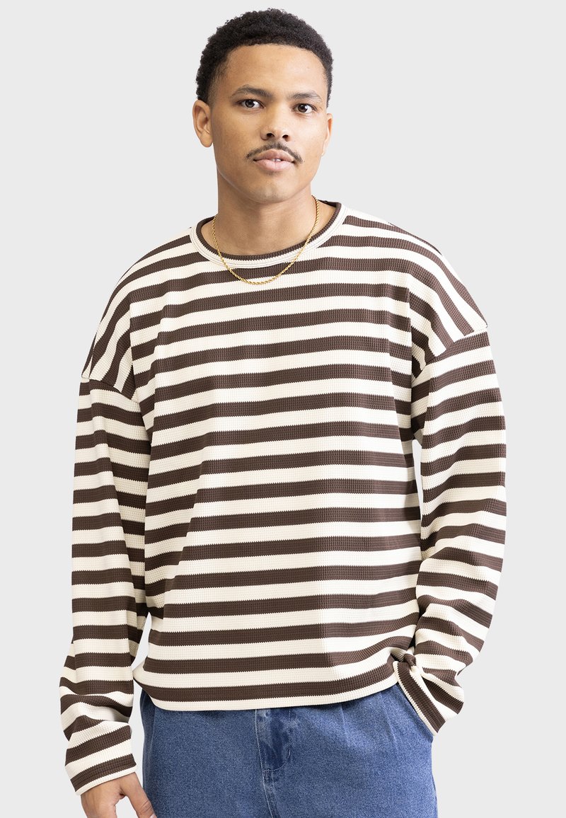 Bruine en crèmekleurige gestreepte lange mouwshirt in een textuurstof, met een relaxte pasvorm en geribbelde halslijn, gedragen met blauwe denim broek.
