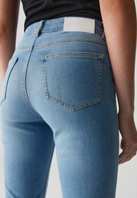 Jeans in denim azzurro chiaro con una texture liscia, dotati di un'etichetta bianca sul retro e due tasche posteriori con contour cucito.