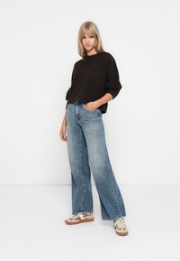 Brun, teksturert strikkegenser med vide ermer, kombinert med lys blå, vide denimbukser. Modellen har på seg beige sneakers med leopardmønster.