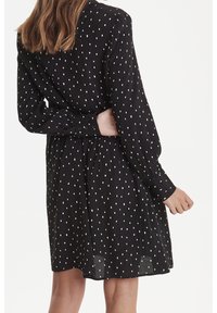 Abito nero a maniche lunghe con pois bianchi, dalla vestibilità morbida e vita arricciata. Il tessuto sembra morbido con una texture leggera.