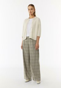 Kardigan w kolorze off-white z krótkim rękawem, zapinany na guziki, w połączeniu z szerokimi spodniami w kratę w odcieniach beżu, zieleni i brązu. Miękka, fakturowana tkanina i luźny krój.