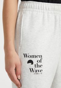 Heledad hallide spordipüksid elastse vöökoha ja musta tekstiga "Women of the Wave", millel on disainielement reie peal.