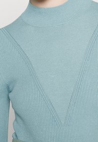 Hellblauer, gerippter Rollkragenpullover mit einem V-förmigen Design und diagonalen Mustern. Glatte Textur und taillierte Silhouette.