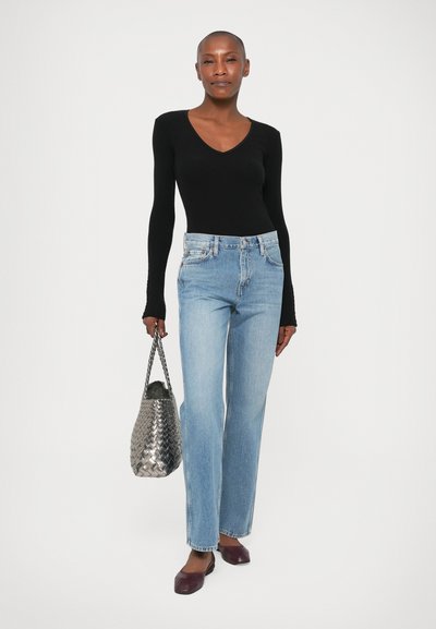 Bodysuit negro de manga larga, jeans de talle alto azul claro, bolso de mano tejido plateado y bailarinas burdeos. Diseño simple y ajustado con acentos mínimos.