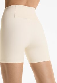 High-waisted beige shorts van rekbaar materiaal. Heeft een gladde textuur, een nette zoom en een subtiel logo op de tailleband.