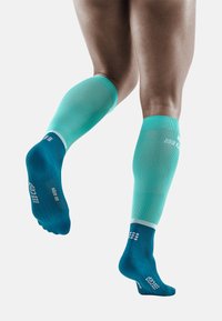 Compressiekousen met een turquoise bovenkant en een donkerblauwe voetzool, met een textuurafwerking en een witte accentrand bij de boord.