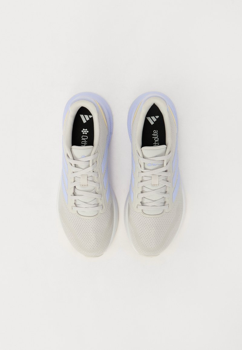 Zapatillas deportivas gris claro con paneles de malla, acentos morados y cordones planos. Plantillas negras con el logotipo de la marca. Suela de goma texturizada.
