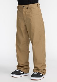 Pantalons de neige kaki avec une coupe droite, fabriqués à partir d'un matériau résistant à l'eau, avec des poches latérales et une boucle de ceinture. Baskets noires visibles.