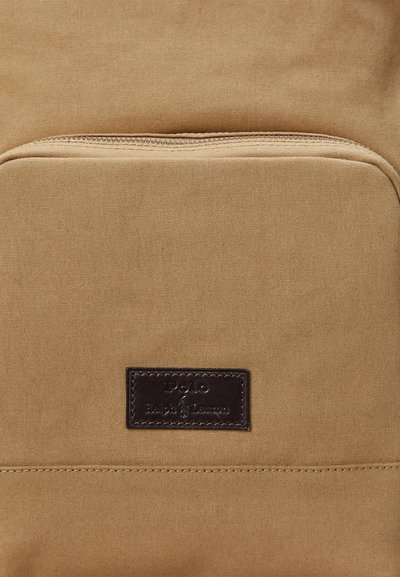 Kapsa na batohu z látky v hnedomodrom odtieni s viditeľným zipsom a malou tmavohnedou koženou záplatou s vyrazeným logom Polo Ralph Lauren.