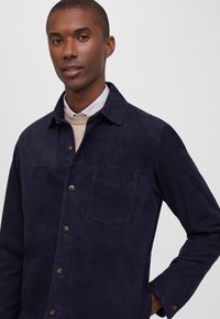 Chaqueta de camisa de ante azul marino con cuello, cierre delantero de botones, bolsillo en el pecho y mangas largas con puños abotonados.