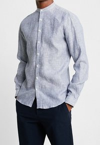 Camicia a maniche lunghe a righe blu e bianche con colletto alla mandarino, caratterizzata da bottoni bianchi e un tessuto morbido e testurizzato.