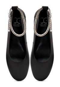 Bailarinas negras con un acabado de cuero sintético suave. Presentan detalles en cadena plateada en el talón. Diseño de punta redonda, estilo minimalista.