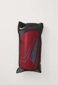 Red and blue Nike Mercurial shin guards in a black mesh storage bag, featuring a prominent Nike logo at the top and large size indicator.