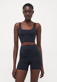 Tamno plavi sportski crop top i kratke hlače visokog struka napravljeni od rastezljivog materijala, s prilagođenim dizajnom i minimalističkom konstrukcijom.