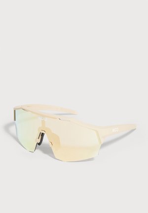 Lunettes de sport enveloppantes à monture beige, verre miroir continu et plaquettes de nez ajustables sur un fond uni.