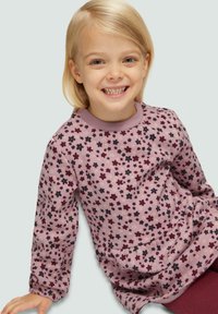 Haut rose clair à manches longues avec encolure ronde, présentant un motif floral en violet foncé et noir. Tissu doux avec coupe décontractée.