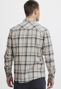 Camicia a maniche lunghe a quadri nei colori crema, blu e beige. Presenta un colletto a bottoni e uno yoke posteriore strutturato, realizzata in tessuto morbido e testurizzato.