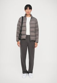Nafukovacia bunda v tmavošedej farbe, prešívaný dizajn, vysoký golier, spárovaná so šedými nohavicami a bielymi teniskami, s malou čiernou crossbody taškou.