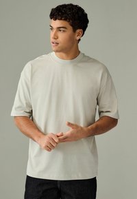 Lys grå kortærmet T-shirt med rund halsudskæring og afslappet pasform, glat tekstur og minimale syningsdetaljer. Båret med mørke jeans.
