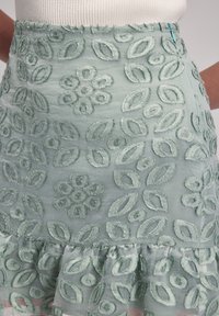 Falda bordada en verde claro, con patrones florales y de hojas. Tejido texturizado con dobladillo con volantes, cierre de cremallera en la parte posterior.