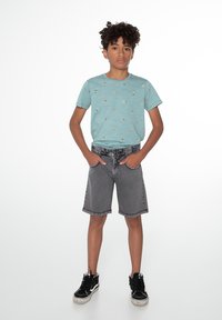 Šviesiai mėlyna marškinėliai su mažais spalvingais raštais, derinami su pilkais džinsiniais šortais ir juodais sportbačiais. Paprastas dizainas, kasdienis siluetas.