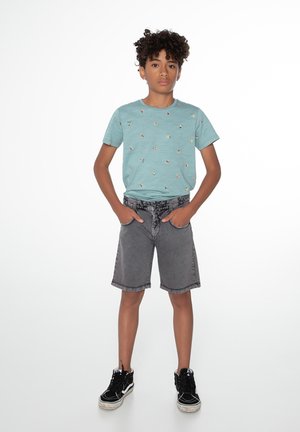 T-shirt azzurro chiaro con piccole stampe colorate, abbinato a pantaloni corti in denim grigi e sneakers nere. Design semplice, vestibilità casual.