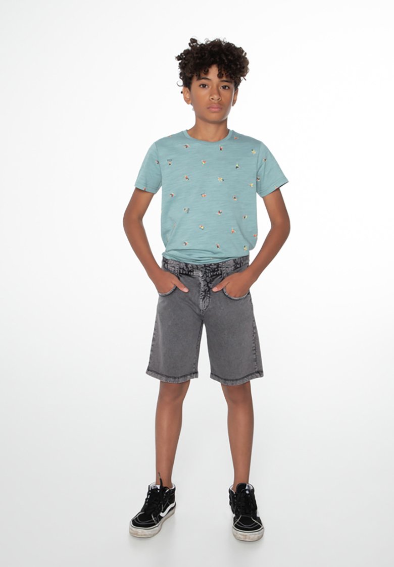 Šviesiai mėlyna marškinėliai su mažais spalvingais raštais, derinami su pilkais džinsiniais šortais ir juodais sportbačiais. Paprastas dizainas, kasdienis siluetas.